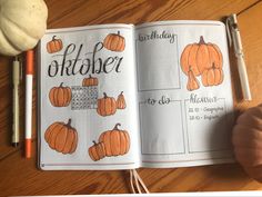 an open notebook with pumpkins on it and a hand holding a pen next to it