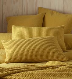 a bed with yellow linens and pillows on top of it, next to a wooden headboard