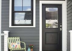 a bench sitting in front of a gray house with a black door and window on the side