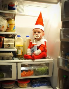 a baby in an elf costume is sitting on top of the refrigerator and drinking milk