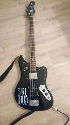 an electric bass guitar laying on the floor with its strap around it's neck