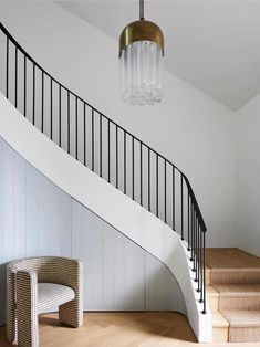 a white staircase with glass chandelier and wicker chair