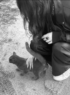 a woman kneeling down petting a cat on the ground