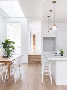 a kitchen with white walls and wooden flooring next to a dining room table filled with chairs