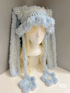 a white mannequin head wearing a light blue hat with ears and pom poms