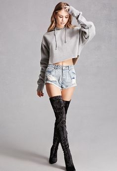 a woman in high waisted shorts and boots posing for the camera with her hands on her head