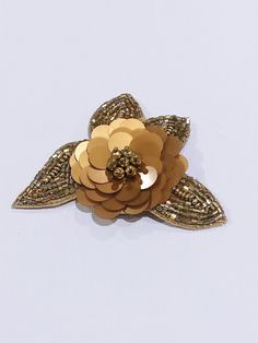 a gold flower brooch sitting on top of a white surface with sequins