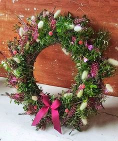 a wreath with pink ribbon hanging on a wooden wall next to a piece of wood