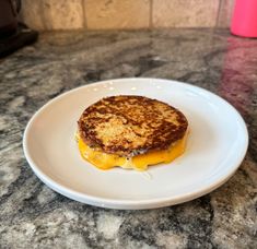 a grilled cheese sandwich on a white plate sitting on a granite counter top next to a pink cup