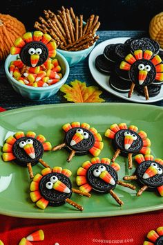 cookies decorated to look like turkeys are on a green platter with candy sticks