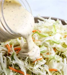 dressing being poured onto a salad with lettuce, carrots and coleslaw