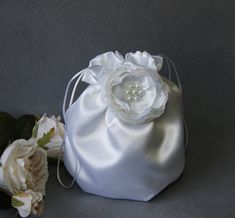 a white satin bag with flowers on the side and one flower in the middle, sitting next to it