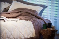 an unmade bed with pillows and blankets on it, next to a wooden stump