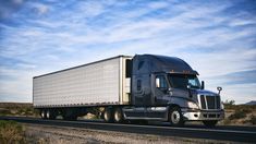 a semi truck driving down the road in the middle of the desert with blue sky and clouds