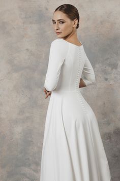 a woman in a white dress is standing with her back turned to the camera and looking off