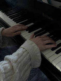 a woman is playing the piano with her hands on it and she is wearing a white sweater