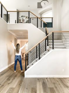 a woman standing in the middle of a living room next to a stair case and clock