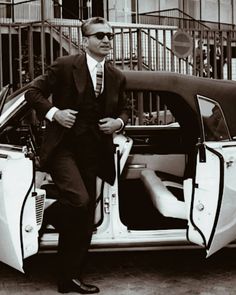 a man in a suit and tie standing next to a car with its door open