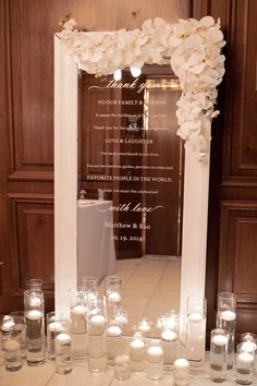 a table with candles and flowers on it in front of a large framed sign that reads,