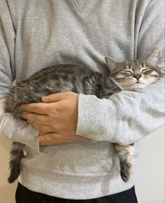 a man holding a cat in his arms while wearing a gray sweater and black pants