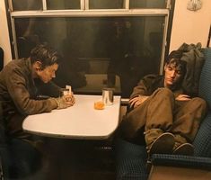 two people sitting at a table in a train car, one is holding a cup