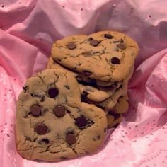 three chocolate chip cookies sitting on top of a pink cloth