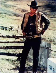 an old photo of a man wearing a cowboy hat and standing in front of a fence