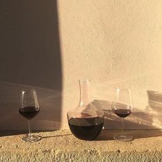 three wine glasses sitting next to each other on a stone ledge in front of a white wall