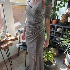 a woman in a gray dress standing next to a potted plant and looking at the camera