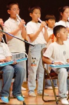 a group of children sitting on chairs with toothbrushes in their mouths