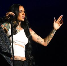 a woman with tattoos on her arms and chest holding a microphone in front of her