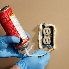 a person in blue gloves is holding a can of spray paint and an electrical outlet