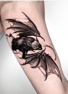 a black and white photo of a dragon tattoo on the leg, with wings spread out