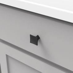 a close up of a black knob on a white cabinet door with an open drawer