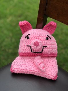 a crocheted pink bear hat and scarf sitting on top of a wooden chair