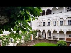 an old building with many windows and balconies on the second floor is surrounded by greenery