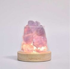 a glass container filled with pink rocks on top of a wooden stand and white background