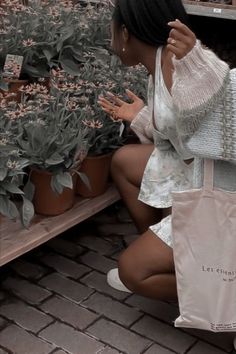 a woman sitting on the ground next to potted plants and holding a shopping bag