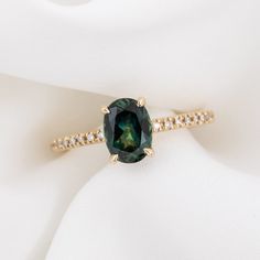 a close up of a ring with a green stone on it's side and diamonds around the band