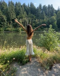 a woman standing in front of a lake with her arms outstretched