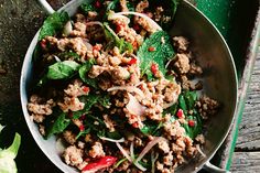 a pan filled with meat and vegetables on top of a wooden table next to lettuce