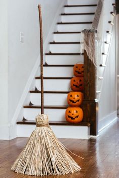 a broom sitting on top of a hard wood floor next to a stair case filled with pumpkins