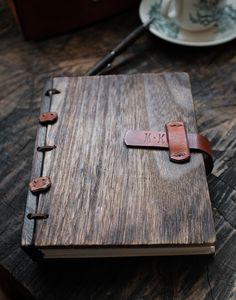 a wooden book with leather straps on top of a table next to a cup and saucer