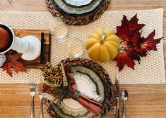 the table is set for thanksgiving dinner with plates, silverware and autumn leaves on it