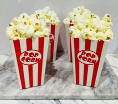 two red and white striped popcorn buckets sitting on a marble slab