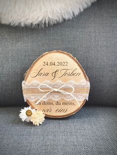 a wooden slice with the names of two people on it and a daisy sitting next to it