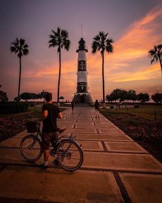 a man is standing next to his bike in front of a lighthouse with palm trees