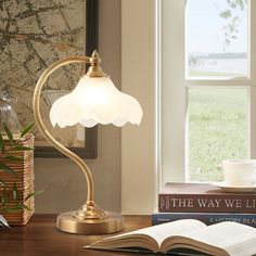 a desk lamp sitting on top of a wooden table next to a book and cup