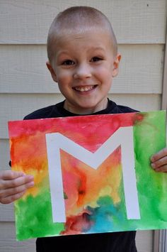 a young boy holding up a paper letter m with the letter m painted on it