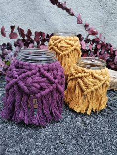 two jars with yarn wrapped around them sitting on the ground next to some purple and yellow flowers